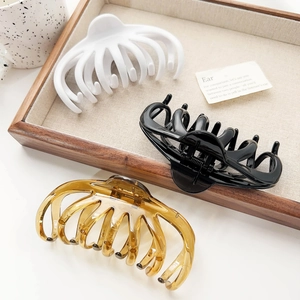 Three large hair claws in white, black, and amber displayed on a wooden tray