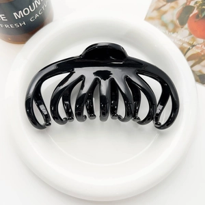 Macro view of a glossy black octopus hair claw clip on a white ceramic plate