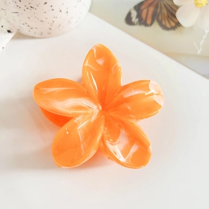 Macro view of orange marble-patterned frangipani hair claw clip on minimalist background