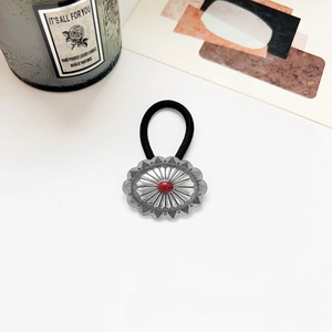 Detail of vintage silver sunflower hair tie with a red stone on a white surface