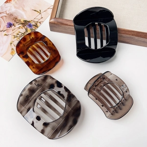 Close-up of four large flat circular hair claws in black, tortoiseshell, grey and amber