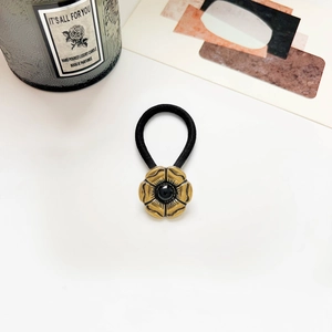 Close-up of a vintage elastic hair tie with a gold floral charm and black bead detail
