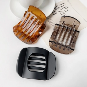 Detailed view of large amber, grey, and matte black shark hair clips on a white desk
