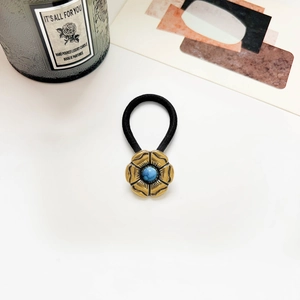 Close-up of vintage golden flower hair tie with a blue turquoise stone on white desk