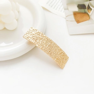 Detail of golden rectangular hair clip with unique wrinkled metal texture on white tray