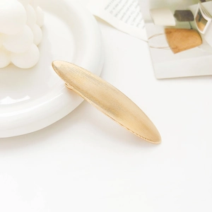 Detailed view of golden oval hair clip with brushed metal texture and sleek finish