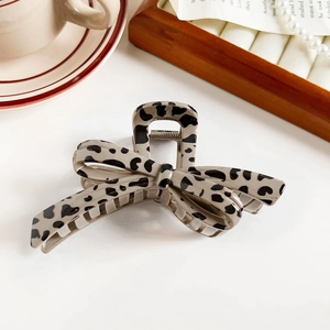 Detail of a leopard print bow hair claw clip styled with pearls on a wooden tray