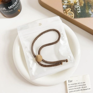 Macro shot of a dark brown elastic hair tie with a textured gold button in polybag