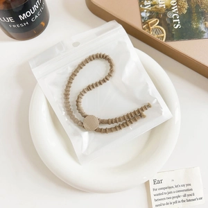 Close-up of brown elastic hair tie with golden textured bead in translucent zipper pouch