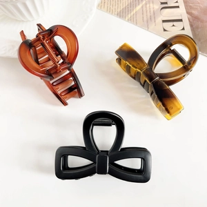 Three elegant bow hair claws in amber and matte black colors on a minimalist background
