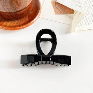 Close-up of a glossy black bow hair claw clip styled on a minimalist warm white desk