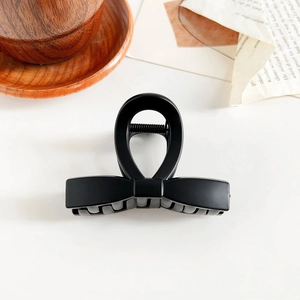 Macro detail of a black matte bow-shaped hair claw clip on a minimalist white surface