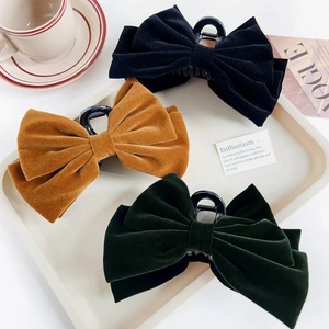Detailed view of velvet bow hair claws in black, yellow, and green on a stylish tray