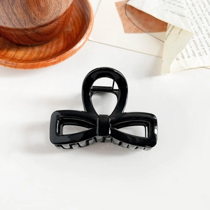 Close-up of a glossy black bow-shaped hair claw clip on vintage book pages