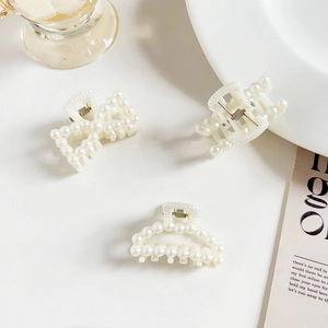 Close-up of three pearl hair claws in rectangular, oval, and bow shapes on a white table