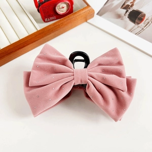 Close-up of pink velvet bow hair claw clip with sparkly rhinestones on wooden tray