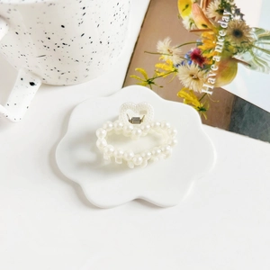 Macro detail of a 4cm pearl heart hair claw clip on a white ceramic display tray