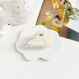 Macro detail of elegant cream hair claw clip with faux pearls on a stylish ceramic tray