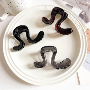Close-up of elegant wavy resin hair claws in black, brown and grey on a ceramic plate