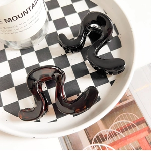 Close-up of wavy S-shaped hair claws in black and tortoise shell on a checkered tray