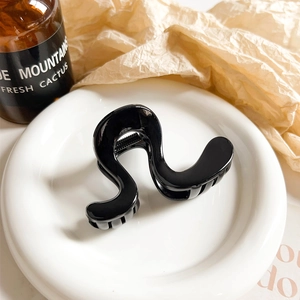 Detail of wavy black hair claw clip with metal spring on a white plate with decor