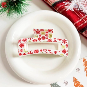 Detail shot of white Christmas hair claw clip with red and gold snowflakes on a festive tray