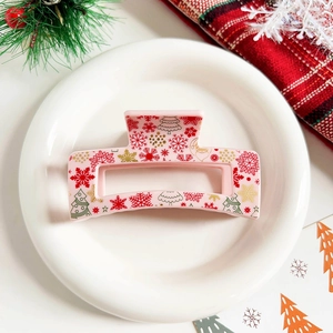Pink Christmas hair claw clip with festive elk and snowflake patterns on a white plate
