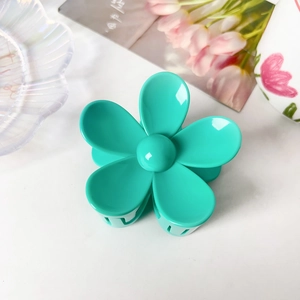 Détail d'une pince à cheveux mate vert citron en forme de fleur sur un plateau blanc