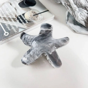 Macro shot of minimalist star-shaped hair claw with grey marble texture on magazine background