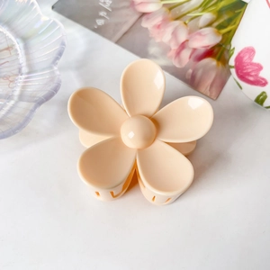 Détail d'une pince à cheveux fleur de 7,5 cm en couleur pêche sur un marbre blanc