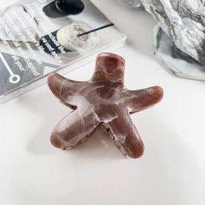 Detailed view of starfish-shaped claw clip with brown marble texture on artistic background