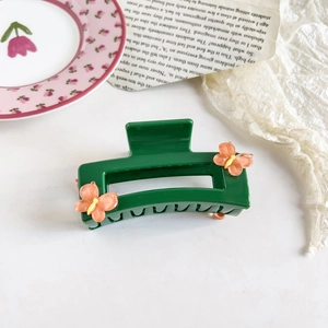 Detail of dark green hair claw clip with orange flower design on marble surface