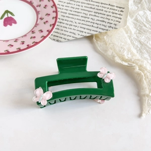 Detailed close-up of a green rectangular hair claw clip with pink 3D butterfly ornaments