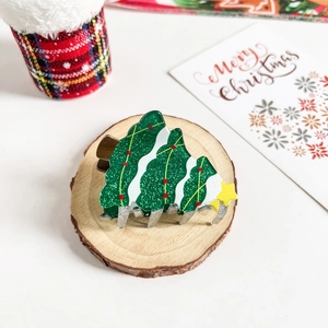 Detail of Christmas tree hair claw clip with green glitter texture and star on a wood slice