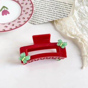 Close-up of a red rectangular hair claw clip with green butterfly floral accents