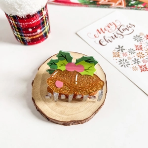 Close-up of a Christmas pudding hair claw clip on a rustic wooden log base for festive styling