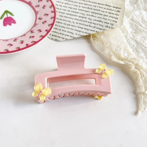 Close-up of pink resin hair claw with yellow butterfly accents on vintage paper