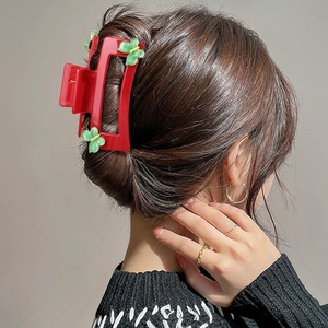 Square red hair claw clip with green flower details worn on a casual updo hairstyle