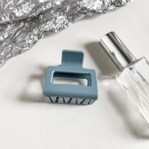 Close-up of a matte dusty blue rectangular hollow hair claw clip on a white surface