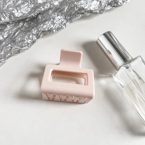 Macro detail of a matte pink square shark hair claw clip with metallic spring on light base