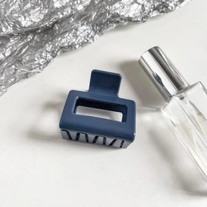 Detail view of navy blue square claw clip with hollow design on silver foil background