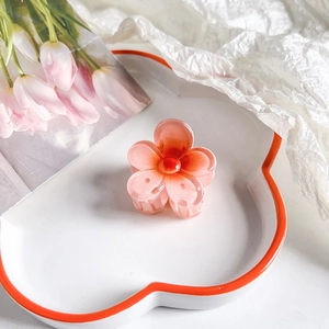Detailed macro view of a pink gradient plumeria flower hair claw on a white ceramic plate