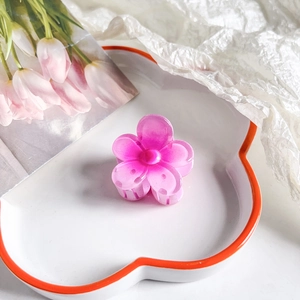 Detail view of a pink resin plumeria hair clip on a white floral ceramic tray