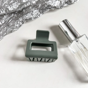 Detail shot of a small sage green square hair claw clip on white and silver background