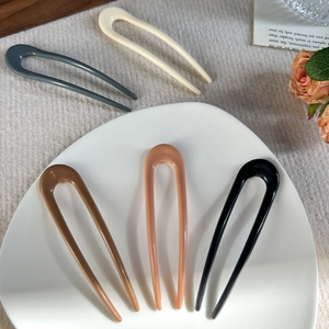 Minimalist U-shaped hair forks in various colors arranged on a white ceramic dish