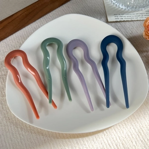 Detail of four colorful wavy U-shaped hair pins on a white plate with aesthetic props