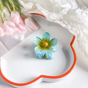 Detail of a light blue plumeria hair claw clip with a glossy jade-like finish on a dish