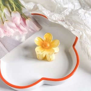 Detail of yellow plumeria hair claw clip on a heart-shaped tray with bright resin finish