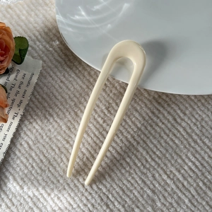 Close-up of minimalist U-shaped cream white hair pin on textured aesthetic background