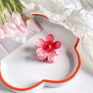 Detail shot of a small pink gradient plumeria hair claw clip on a white ceramic plate
